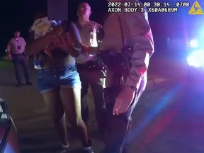 Dans cette capture d'écran d'une vidéo de caméra corporelle de la police, les adjoints du shérif du comté de Los Angeles sont photographiés en train de parler à une mère tenant son bébé quelques instants avant qu'elle ne soit frappée au visage pour avoir refusé de remettre son enfant.