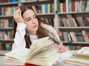 Une adolescente semble distraite alors qu'elle étudie dans une bibliothèque.