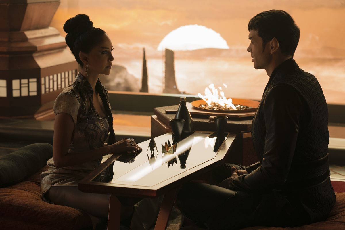 Gia Sandhu dans le rôle de T'Pring et Ethan Peck dans le rôle de Spock sont assis sur des coussins de chaque côté d'une petite table basse dans un restaurant sur Vulcan dans Star Trek : Strange New Worlds. 