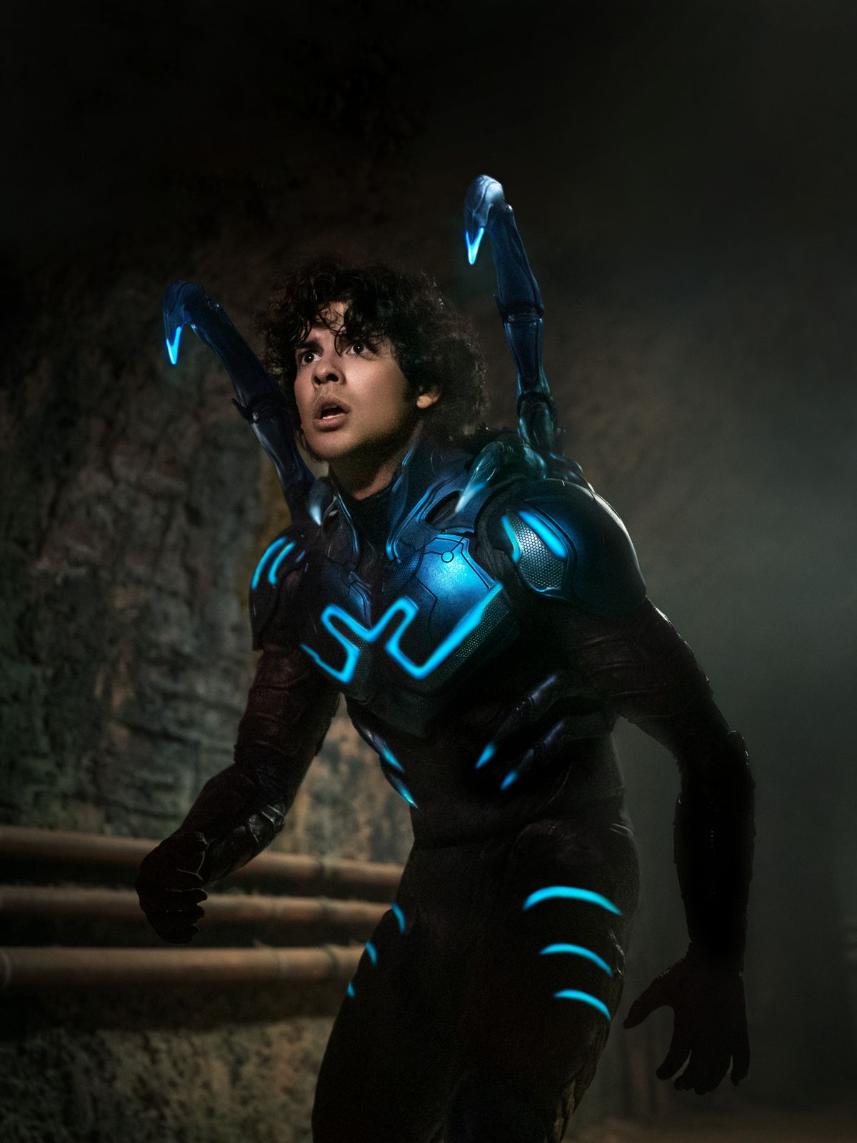 Xolo Maridueña a l'air surpris en portant le costume Blue Beetle devant un mur de pierre en Blue Beetle.