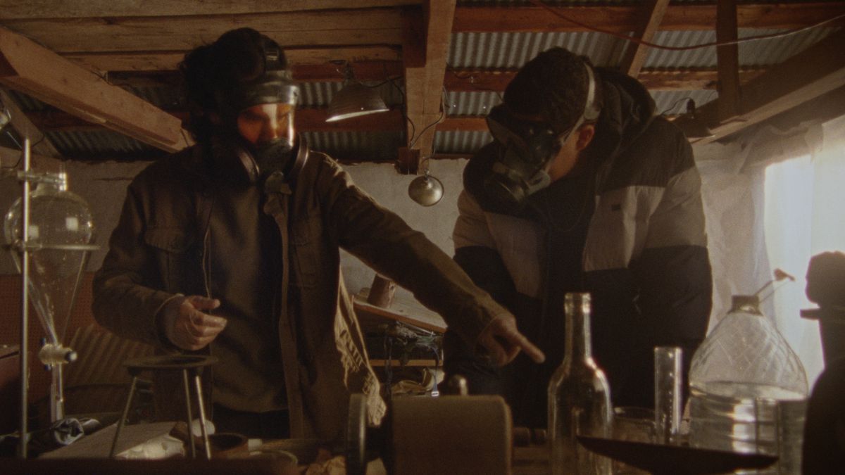 Deux personnes portant des masques à gaz travaillent avec des produits chimiques, tandis que l'une d'entre elles montre comment faire exploser un pipeline.