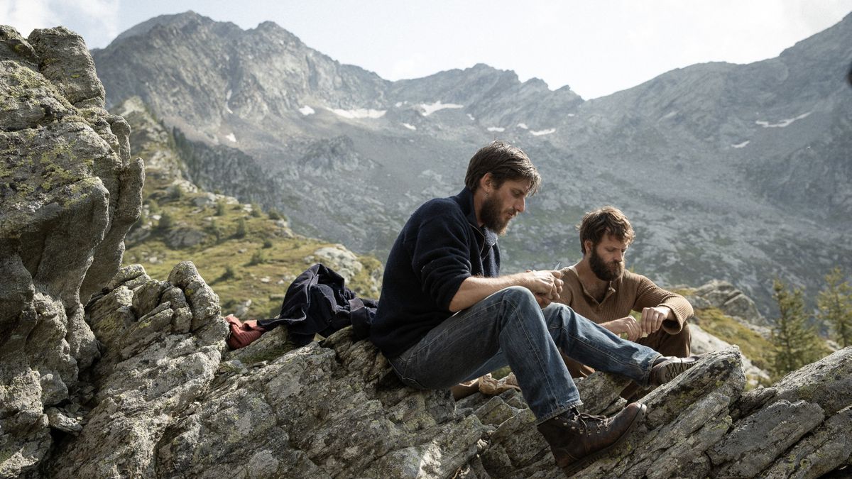 (De gauche à droite) Luca Marinelli et Alessandro Borghi assis sur une montagne surplombant une autre chaîne de montagnes plus grande dans Les Huit Montagnes.