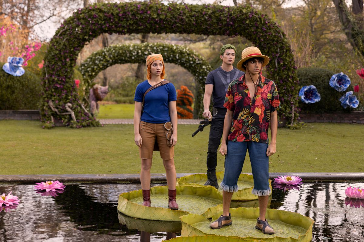 Nami (Emily Rudd), Zoro (Mackenyu) et Luffy (Iñaki Godoy) se tiennent sur des nénuphars dans un jardin coloré dans One Piece de Netflix
