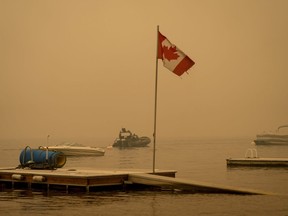 Une épaisse fumée provenant de l'incendie de forêt du Lower East Adams Lake remplit l'air et un drapeau canadien flotte au vent alors que des agents de la GRC patrouillent en bateau sur le lac Shuswap, à Scotch Creek, en Colombie-Britannique, le dimanche 20 août 2023.