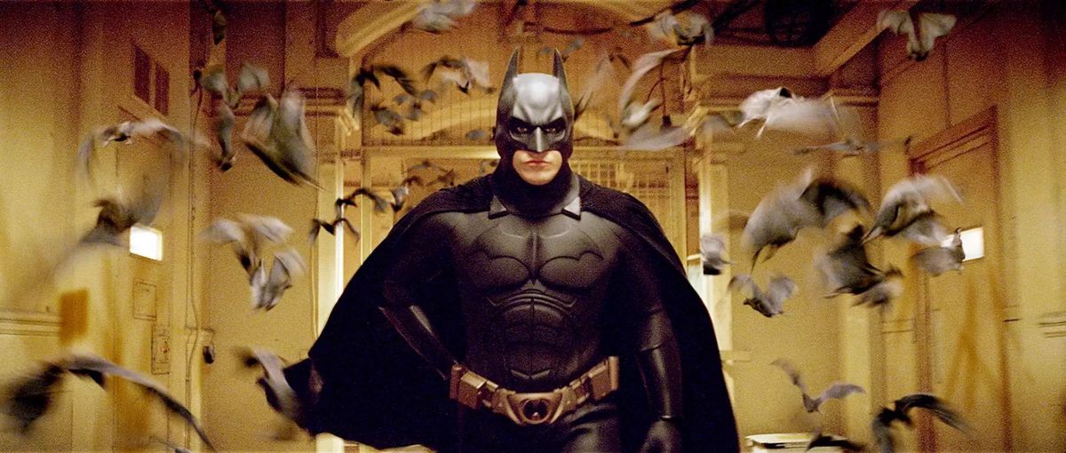 Batman (Christian Bale) traverse un couloir jaunâtre, entouré d'un troupeau de chauves-souris floues et rapides dans Batman Begins de Christopher Nolan
