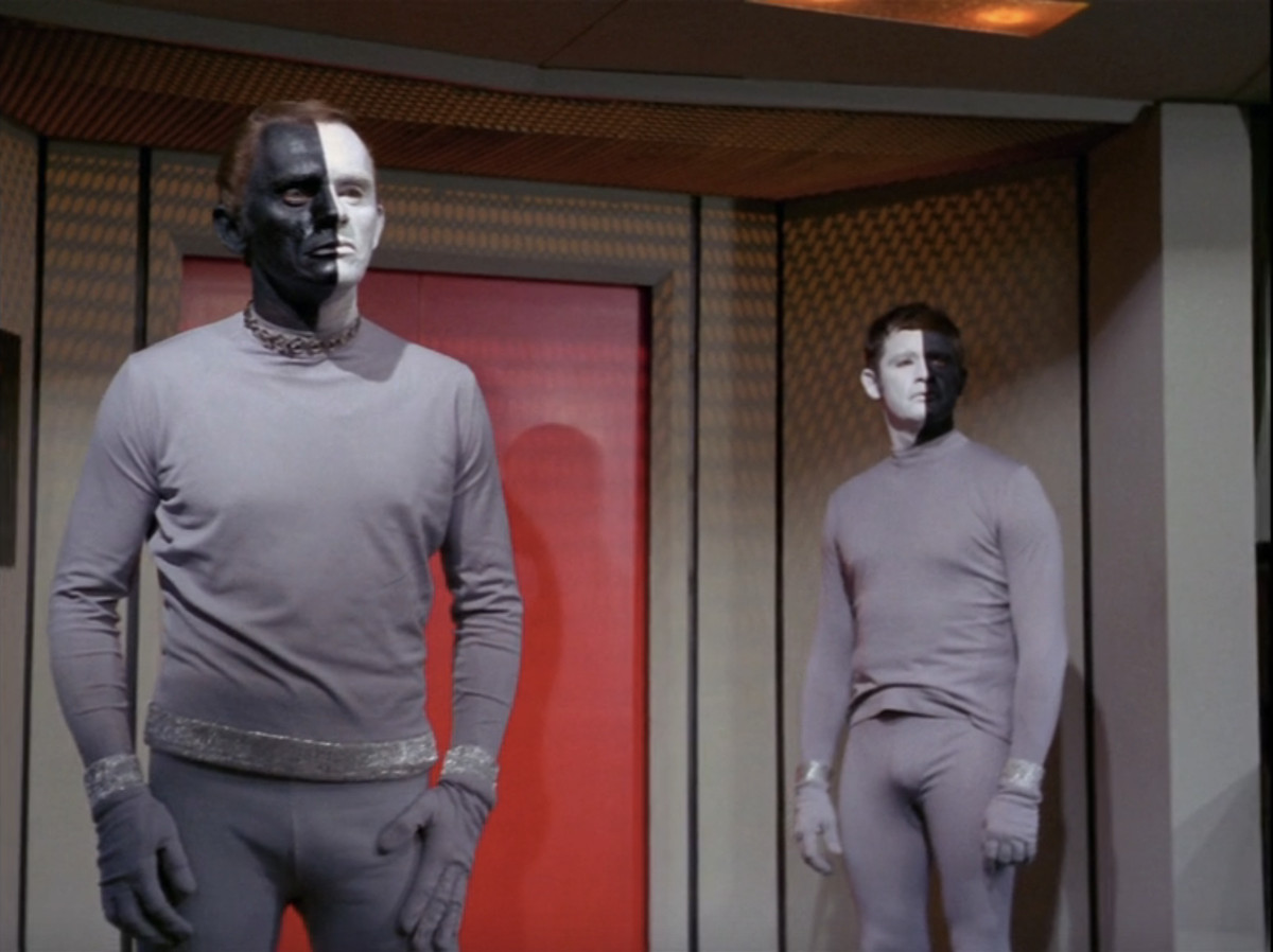 Deux hommes extraterrestres, l'un avec sa moitié gauche noire et sa droite blanche, l'autre inverse, se tiennent sur le pont de l'Enterprise dans une image tirée de l'épisode TOS 