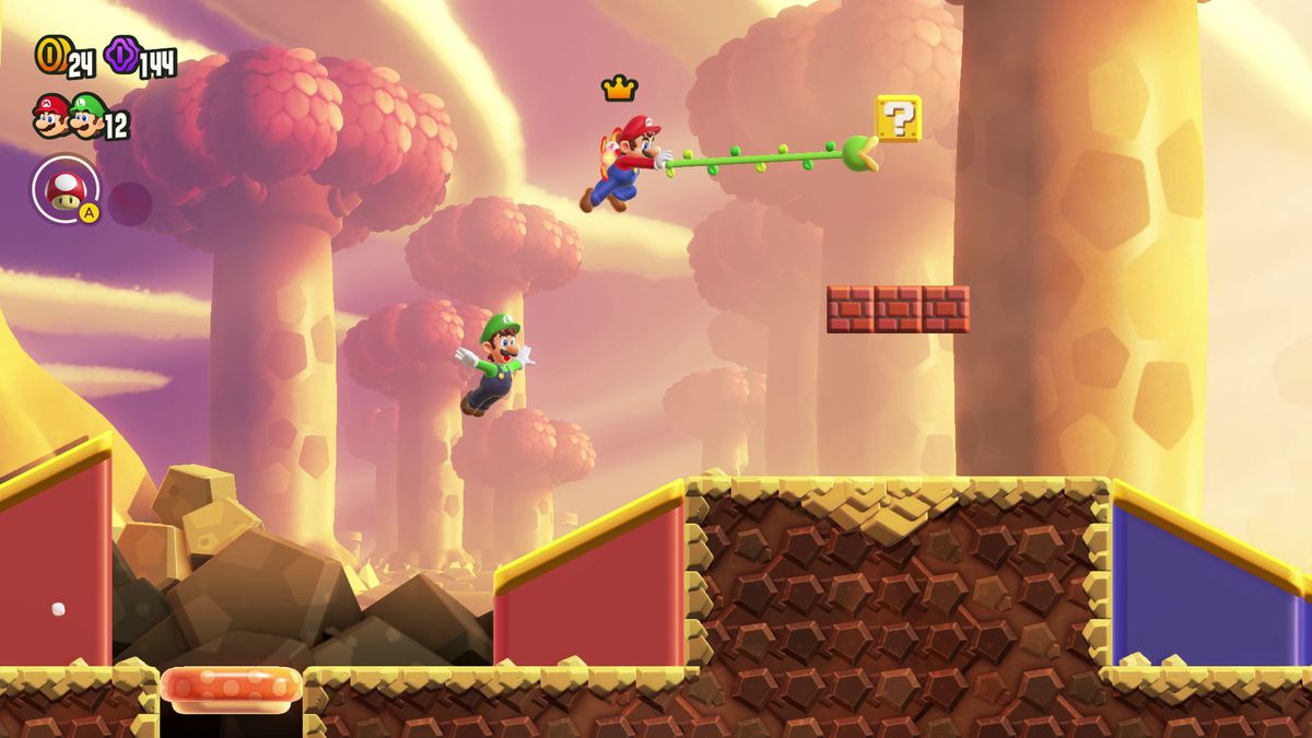 Mario utilise un grappin en forme de vigne pour lire un bloc de questions, avec Luigi sautant derrière lui, dans une capture d'écran de Super Mario Bros. Wonder