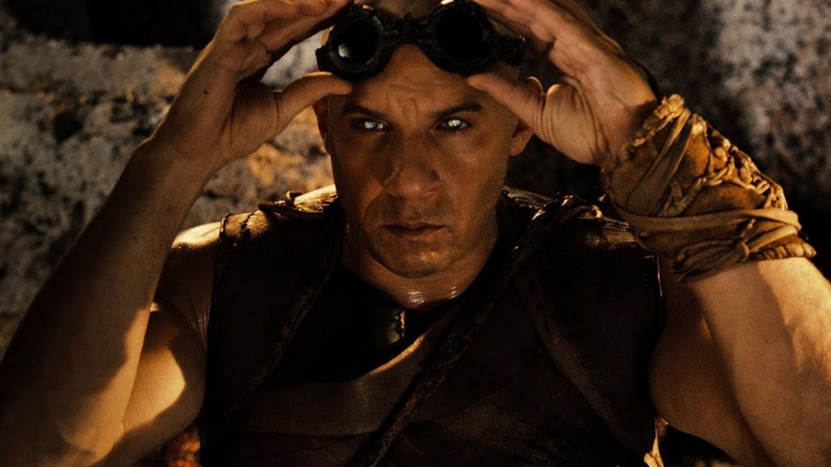 Riddick (Vin Diesel) lève ses lunettes pour révéler ses yeux brillants dans Riddick (2013).