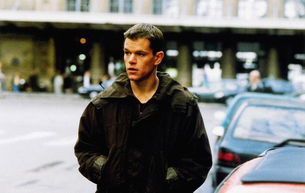 Matt Damon porte une veste vert foncé alors qu'il marche dans une rue de The Bourne Identity.