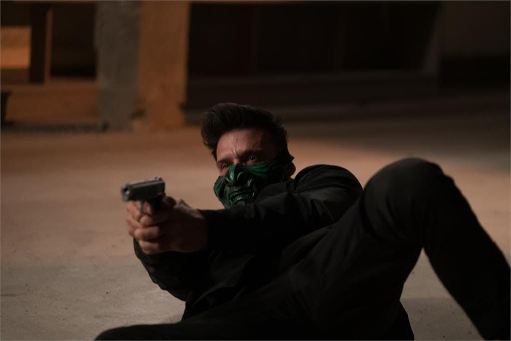 Frank Grillo, portant un masque vert diabolique sur la moitié inférieure de son visage, vise avec une arme à feu alors qu'il est allongé sur le sol dans King of Killers.