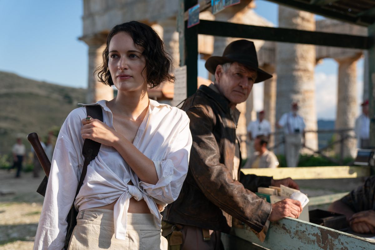 Helena Shaw (Phoebe Waller-Bridge, dans une chemise blanche boutonnée nouée jusqu'au nombril) se tient devant des ruines avec Indiana Jones (Harrison Ford, portant sa tenue classique d'Indiana Jones) dans Indiana Jones et le cadran du destin.