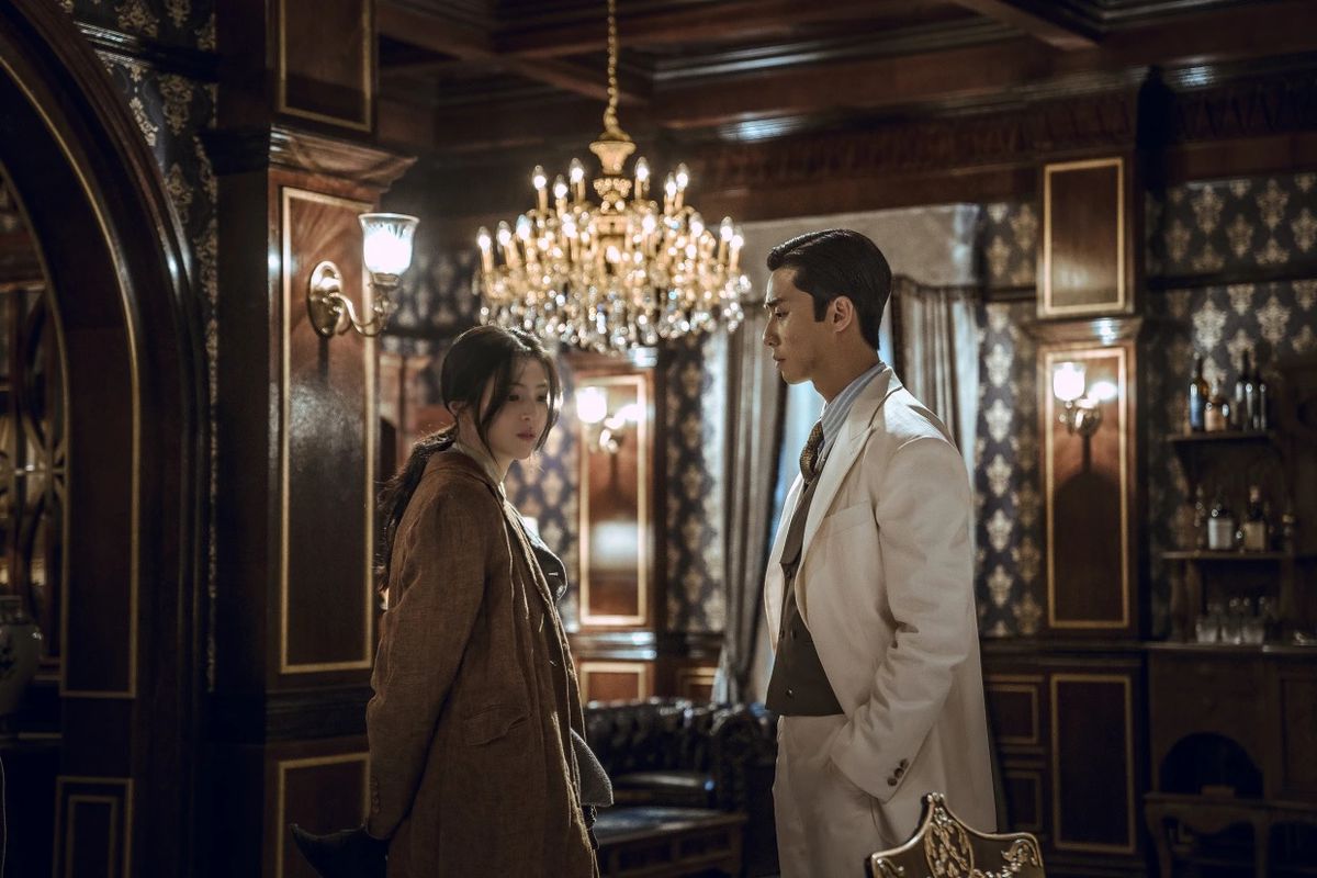 Park Seo-joon et Han So-hee portent de jolis vêtements et se tiennent côte à côte dans une pièce ornée avec un grand lustre dans Gyeongsang Creature.