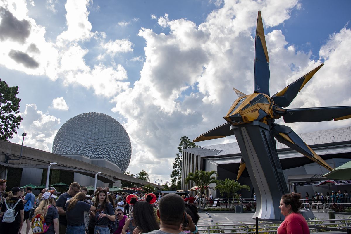 Les visiteurs du parc à thème font la queue pour une balade au parc Epcot de Disney World.  Le célèbre « Epcot Ball », qui abrite le manège Spaceship Earth, est visible en arrière-plan.
