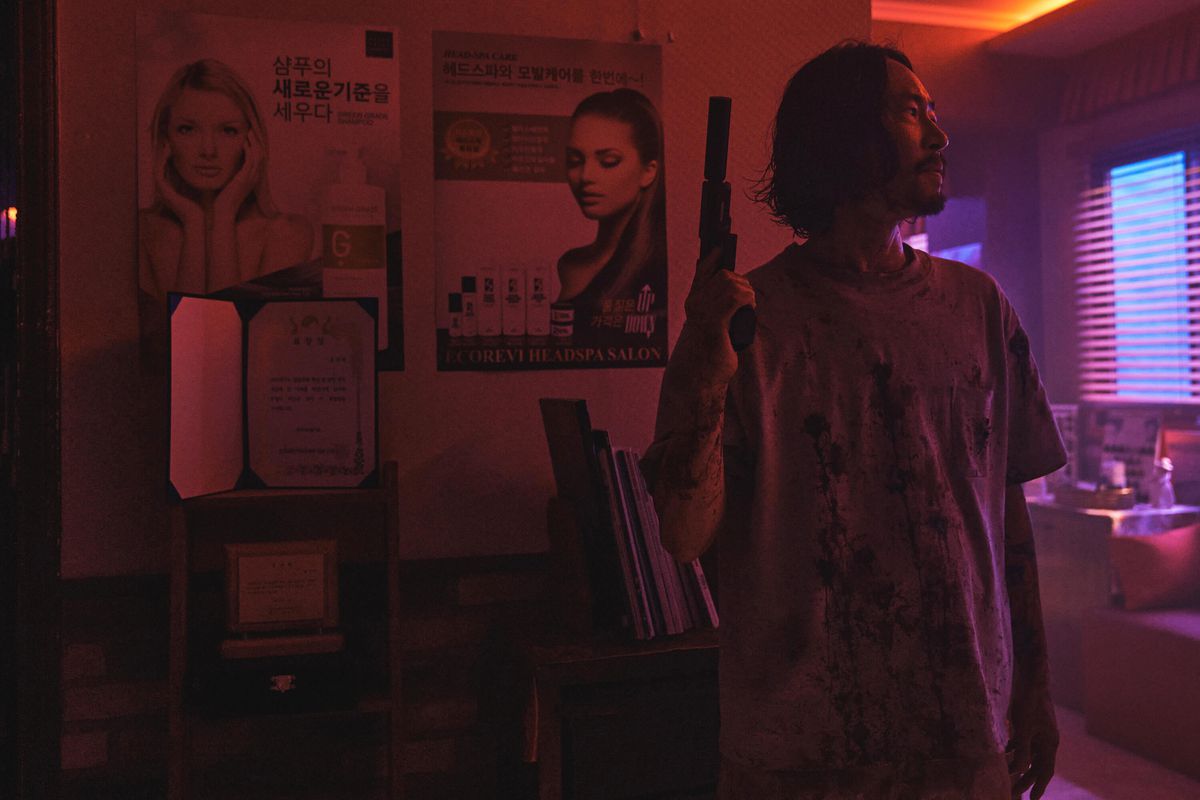 Frank (Ryu Seungbum) debout dans une pièce faiblement éclairée, tenant un pistolet avec un silencieux