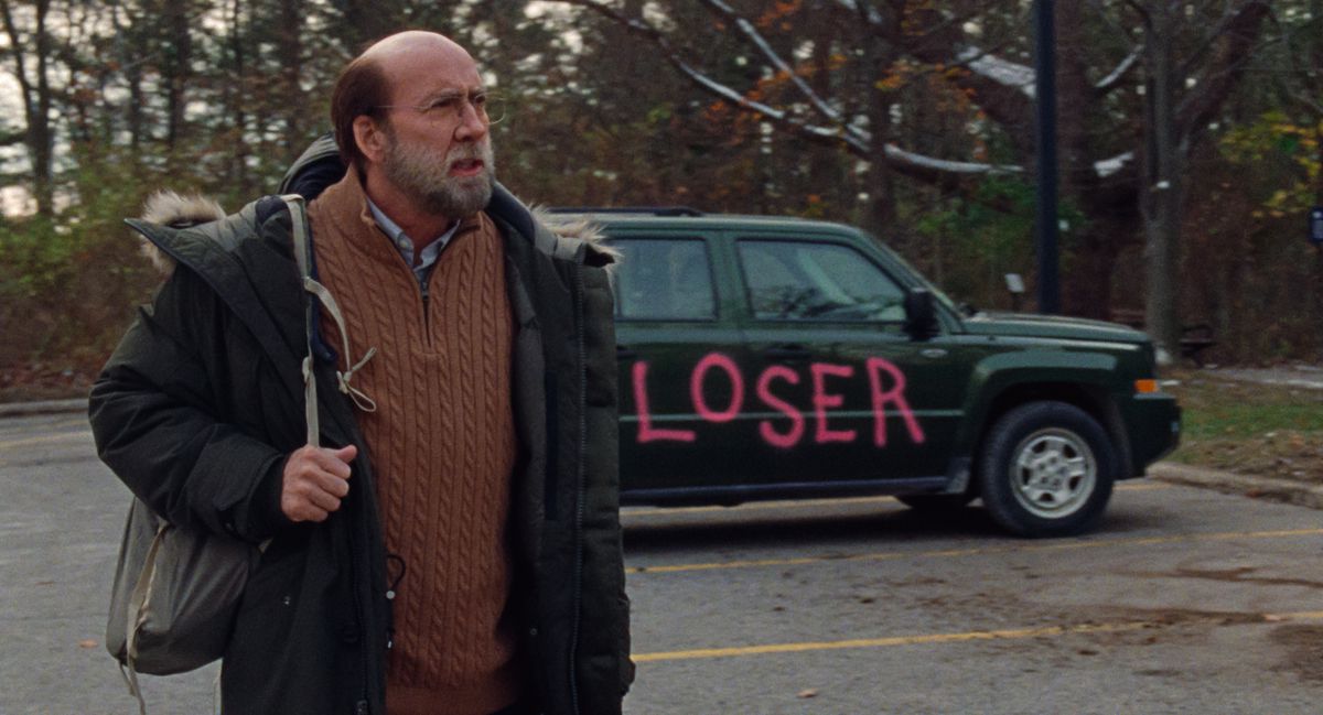 Nicolas Cage, au look schlubby, tient un sac à dos et se tient devant une voiture avec «LOSER» peint dessus en lettres rose vif dans Dream Scenario.