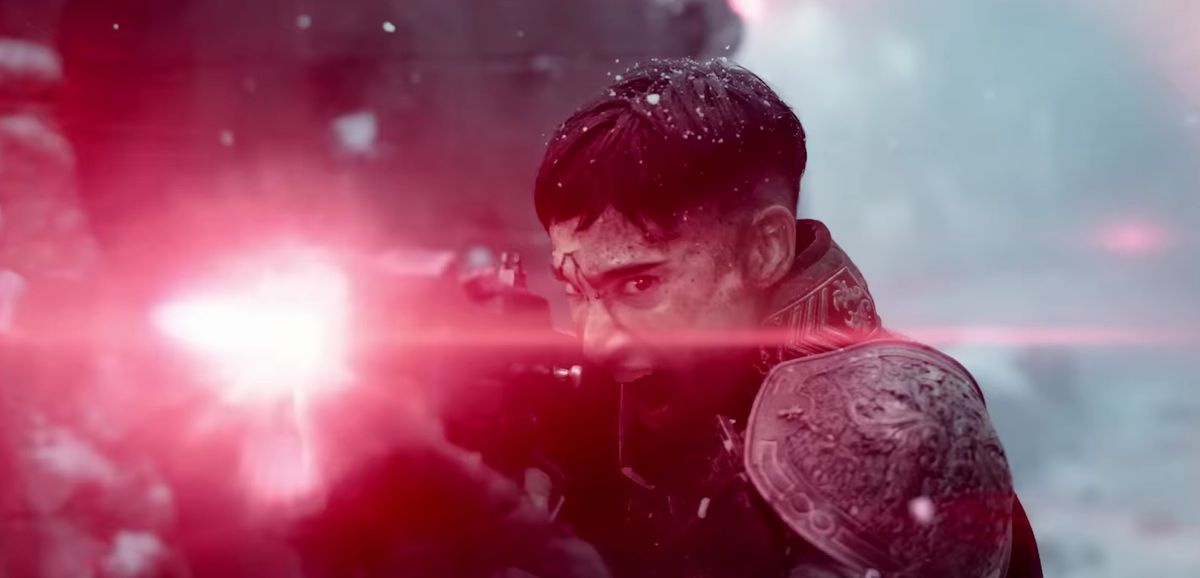 Un personnage aux cheveux noirs vêtu d'une armure complexe tire avec une arme à rayon qui produit une lumière rose vif dans Rebel Moon de Zack Snyder.
