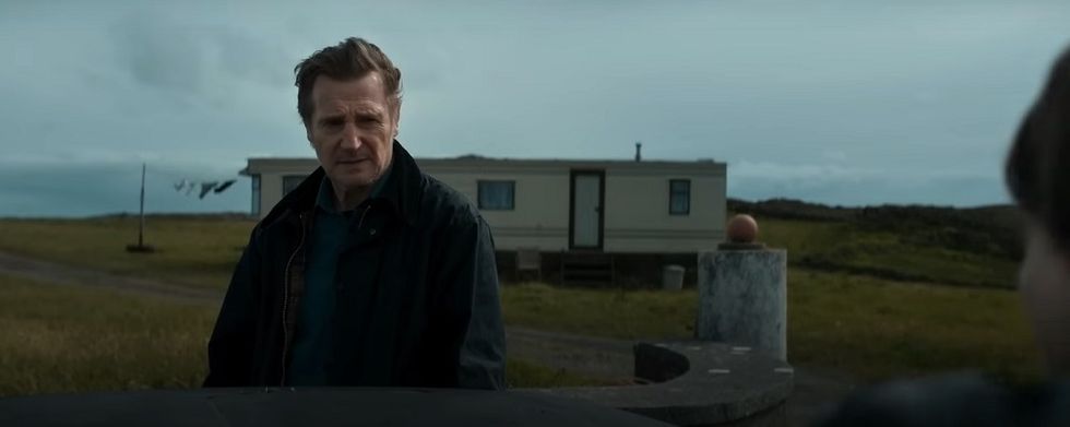 Liam Neeson dans le film Le pays des saints et des pécheurs, son personnage se tient devant une caravane et a l'air inquiet