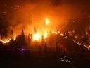 L'incendie de forêt de McDougall Creek brûle à flanc de montagne au-dessus d'une maison au bord d'un lac, à West Kelowna, en Colombie-Britannique, le vendredi 18 août 2023.