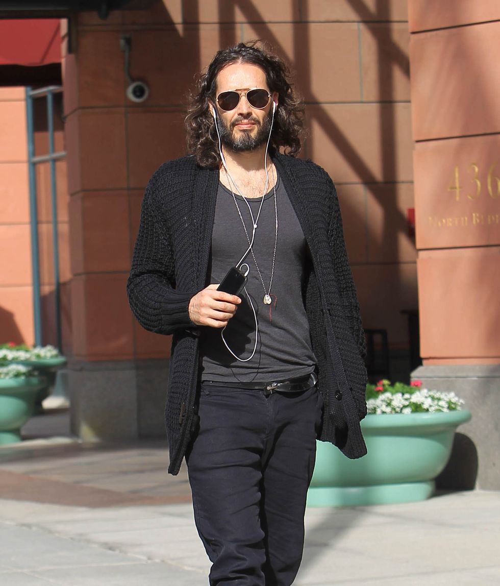 La marque Russell photographiée en 2018 marchant dans la rue, il porte des lunettes de soleil et une tenue noire et grise, et a des écouteurs dans les oreilles.