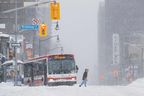 Un piéton traverse la rue alors qu'un autobus urbain est photographié coincé pendant une tempête hivernale à Toronto, le lundi 17 janvier 2022. 