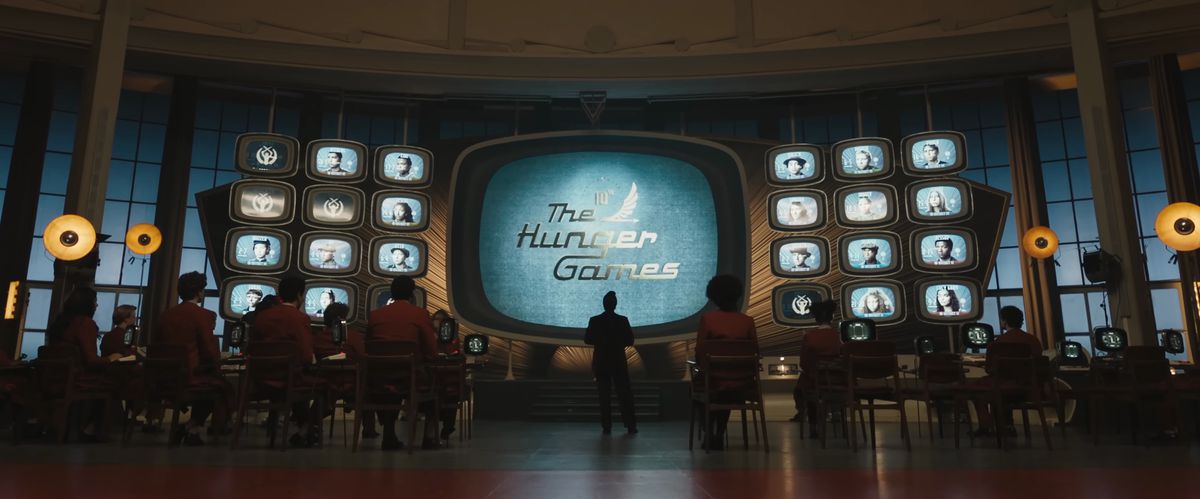 Le logo mondial des Hunger Games sur des écrans de télévision rétro pendant que les employés des jeux réfléchissent à ce qui se passe.