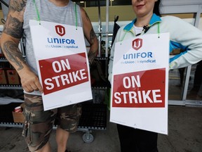 Des travailleurs tiennent des pancartes sur une ligne de piquetage devant une épicerie Metro à Toronto alors que les travailleurs ont rejeté un accord de principe déclenchant une grève de près de 3 700 employés d'épicerie dans la région du Grand Toronto, le samedi 29 juillet 2023.