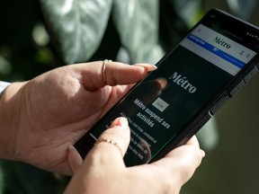 Une personne tient un téléphone affichant la page d'accueil de Metro Media, qui indique en français que l'entreprise suspend ses activités, à Toronto, le vendredi 11 août 2023.