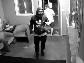 Image de caméra de surveillance en noir et blanc d'un homme portant un sweat à capuche Adidas entrant dans le hall d'un motel.