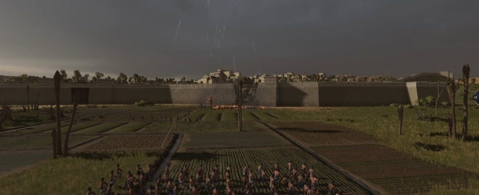 Total War Pharaoh review: A group of slingshoters stand before a broken city wall as enemy units pour our for a counterattack.