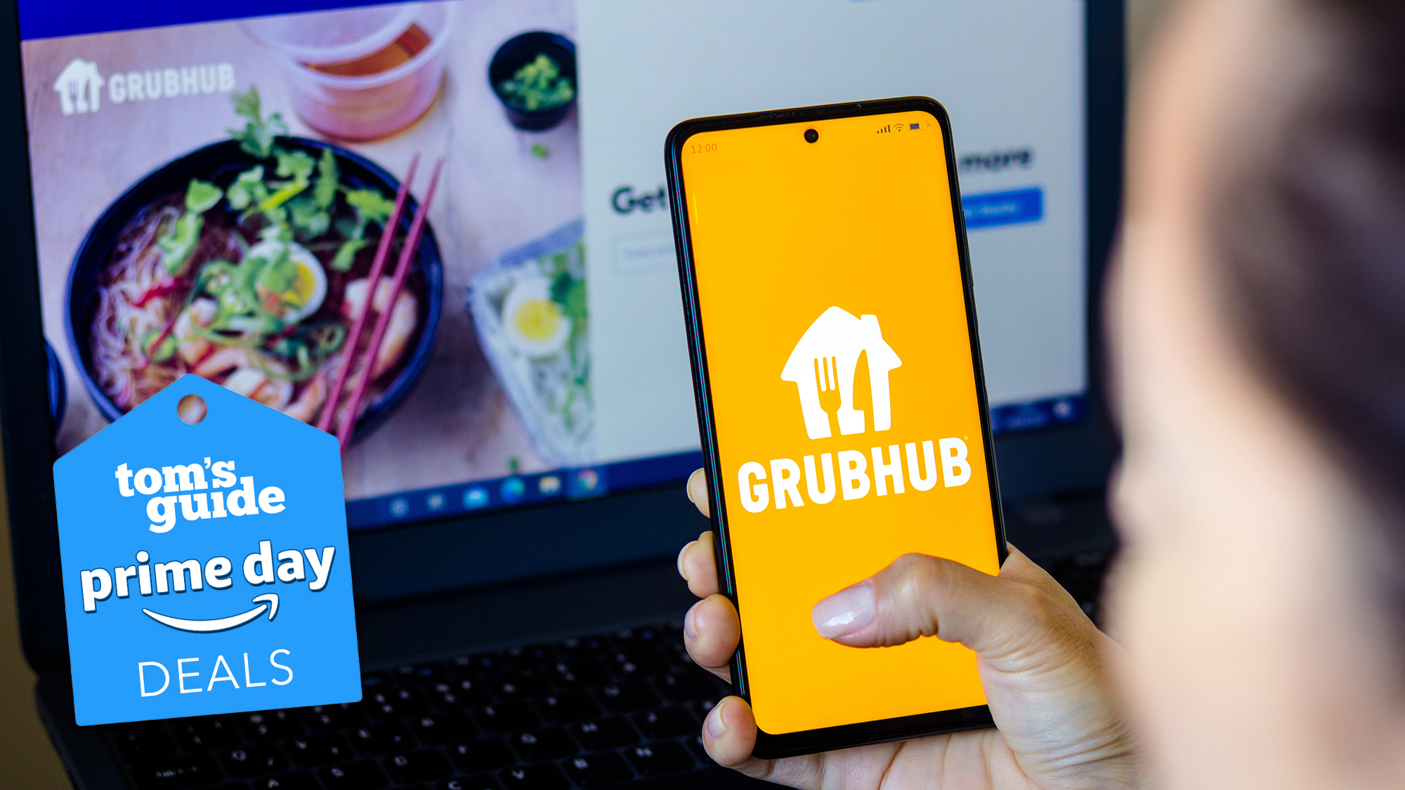 Un téléphone avec un logo Grubhub est en main au-dessus d'un ordinateur portable avec le site Grubhub