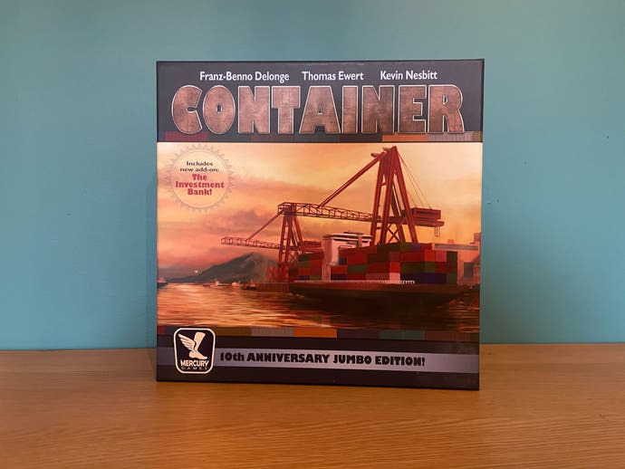 La boîte du jeu de société Container (Jumbo Edition), qui est un jeu sur les porte-conteneurs.  Il montre une image aux couleurs du coucher du soleil d’un porte-conteneurs embarquant une cargaison.  Scintillant.