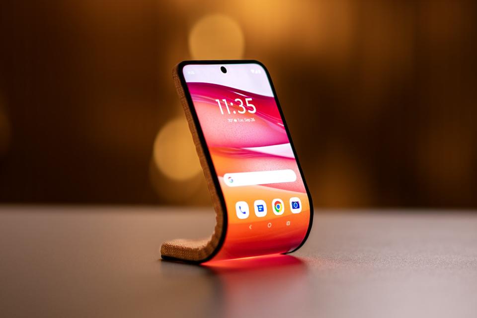 Une image marketing de Motorola, présentant un téléphone pliable/enroulable.  L'appareil repose sur une table avec sa partie inférieure servant de base et sa partie supérieure (courbée) dépassant vers le haut comme un écran intelligent.
