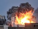 Des gens debout sur un toit regardent une boule de feu et de fumée s’élever au-dessus d’un bâtiment de la ville de Gaza le 7 octobre 2023 lors d’une frappe aérienne israélienne.