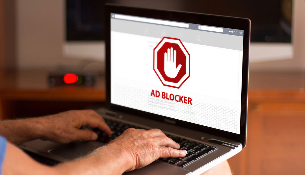 Les mains d'un homme tapent sur un ordinateur portable avec les mots « Ad Blocker » affichés à l'écran.