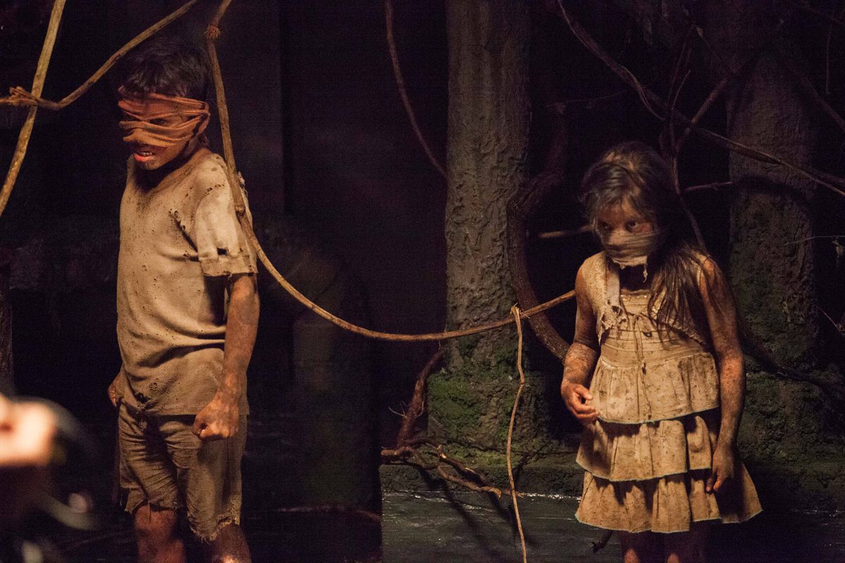 Deux enfants vêtus de vêtements poussiéreux et coiffés d'un bandeau sont attachés par une corde dans From the Dark.