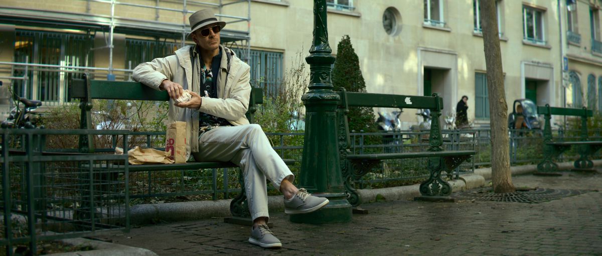Michael Fassbender dans le rôle du Tueur, assis de manière détendue sur un banc, habillé en touriste allemand