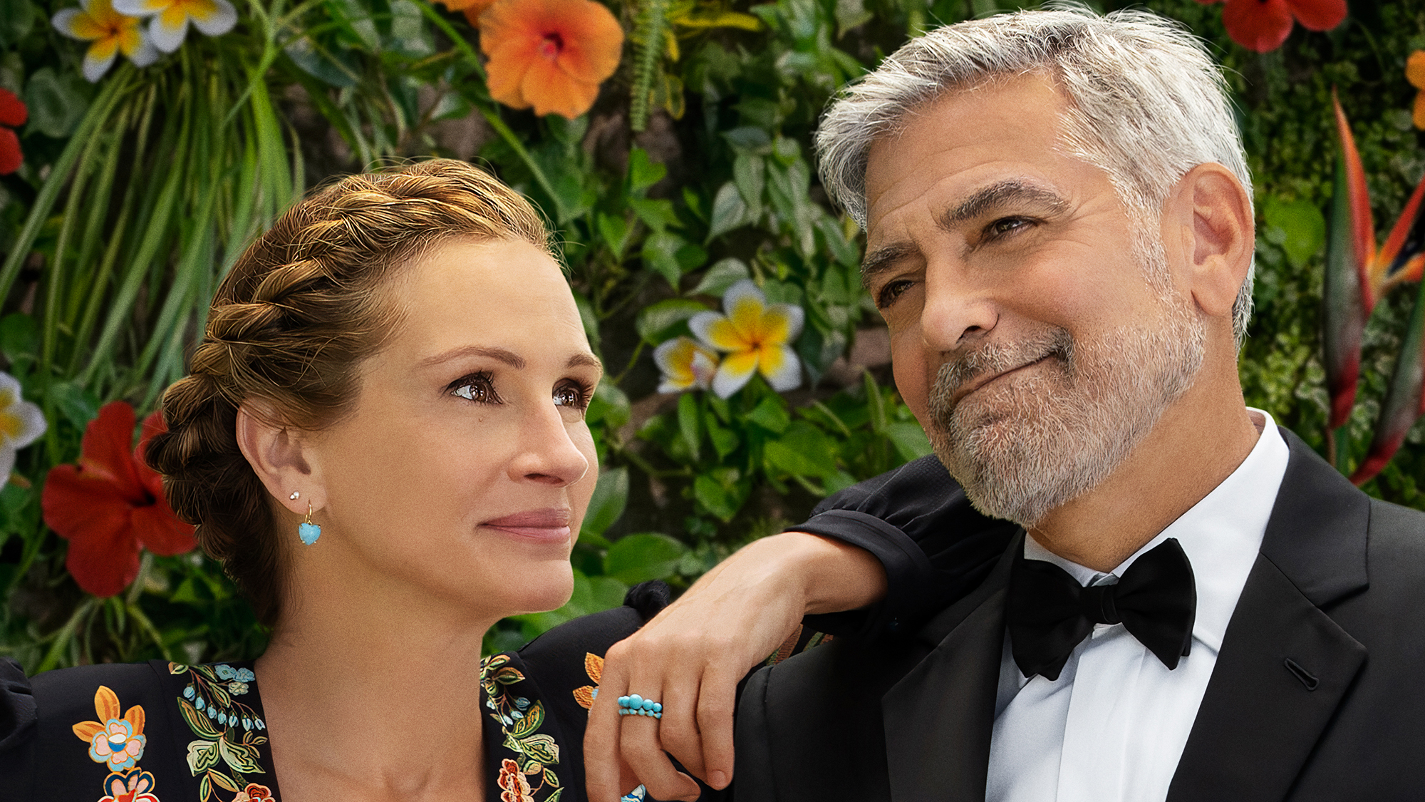 (De gauche à droite) Julia Roberts et George Clooney devant des fleurs sur l'affiche de Ticket to Paradise.