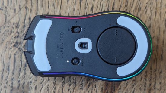 Test du Razer Cobra Pro : une souris noire avec RGB multicolore apparaît à l'envers sur une surface en bois.