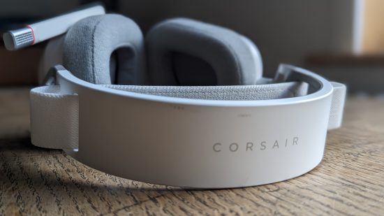 Test du Corsair HS80 Max : un casque blanc avec microphone rétractable apparaît d'en haut sur une table en bois.