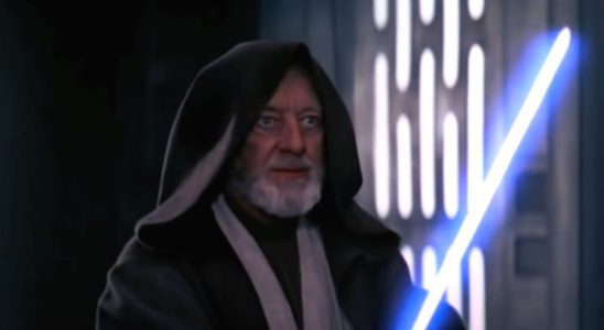 Alec Guinness stands with his lightsaber drawn in Star Wars.