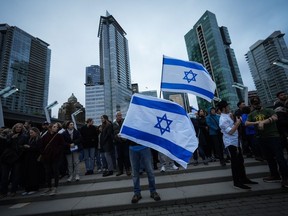 Des gens brandissent des drapeaux israéliens lors d’une veillée organisée par la Fédération juive du Grand Vancouver en soutien aux personnes tuées en Israël, à Vancouver, le mardi 10 octobre 2023.