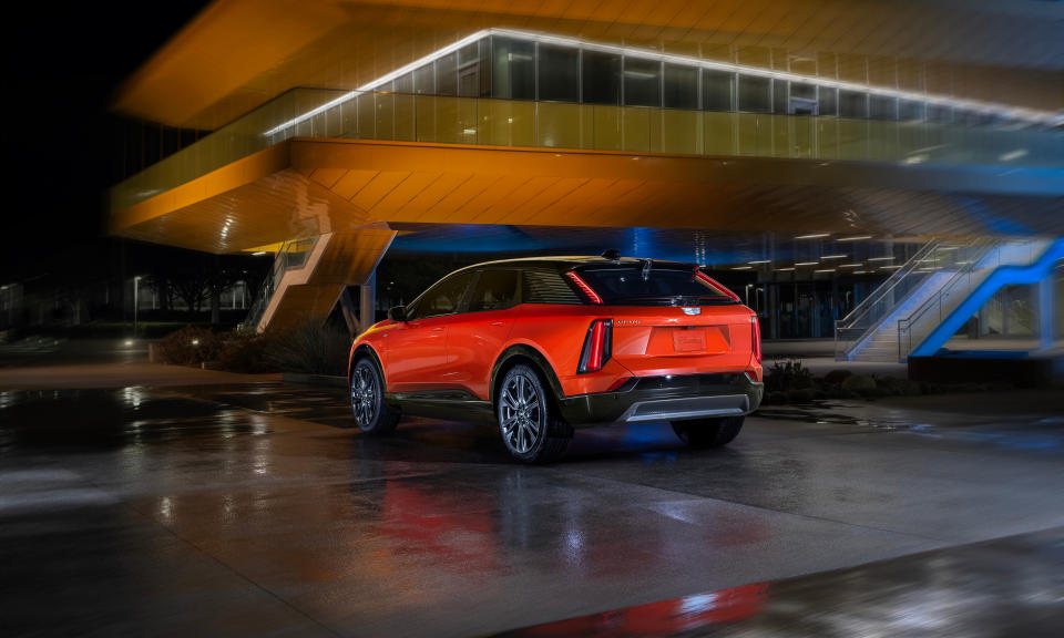 Photo marketing de la Cadillac Optiq, assise sous un immeuble moderne la nuit.  Le véhicule est d'un rouge-orange.