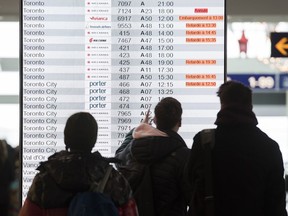 Des passagers regardent un panneau d'information au terminal des départs de l'aéroport Pierre-Elliott-Trudeau de Montréal, le mardi 31 décembre 2019.