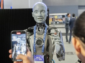 Des gens prennent des photos d'un robot IA lors de la conférence All In sur l'intelligence artificielle à Montréal.