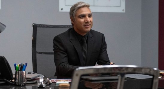 Nick Mohammed as Nate in a black suit sitting at his desk in Ted Lasso.