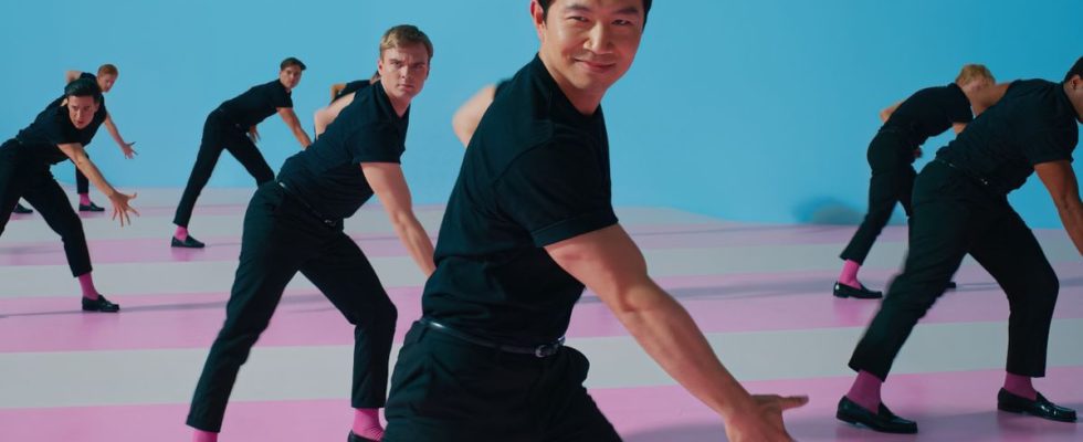 Simu Liu dances with a smirk on his face among a group of fellow Kens in Barbie.