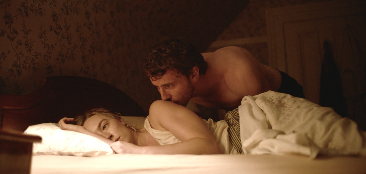 Hen (Saoirse Ronan) est allongée dans son lit, l'air découragée tandis que Junior (Paul Mescal) l'embrasse timidement sur l'épaule.