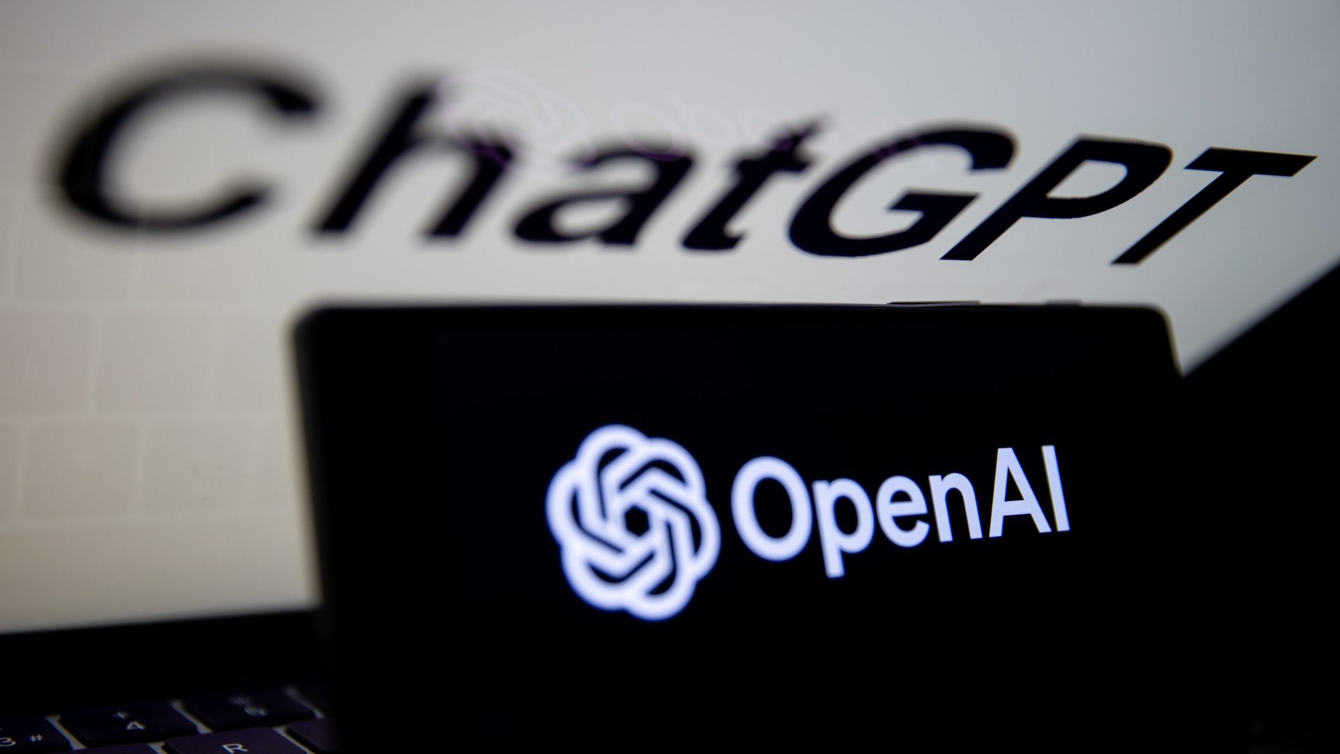 Le logo OpenAI est affiché sur l'écran d'un téléphone mobile devant l'écran de l'ordinateur avec le logo de ChatGPT