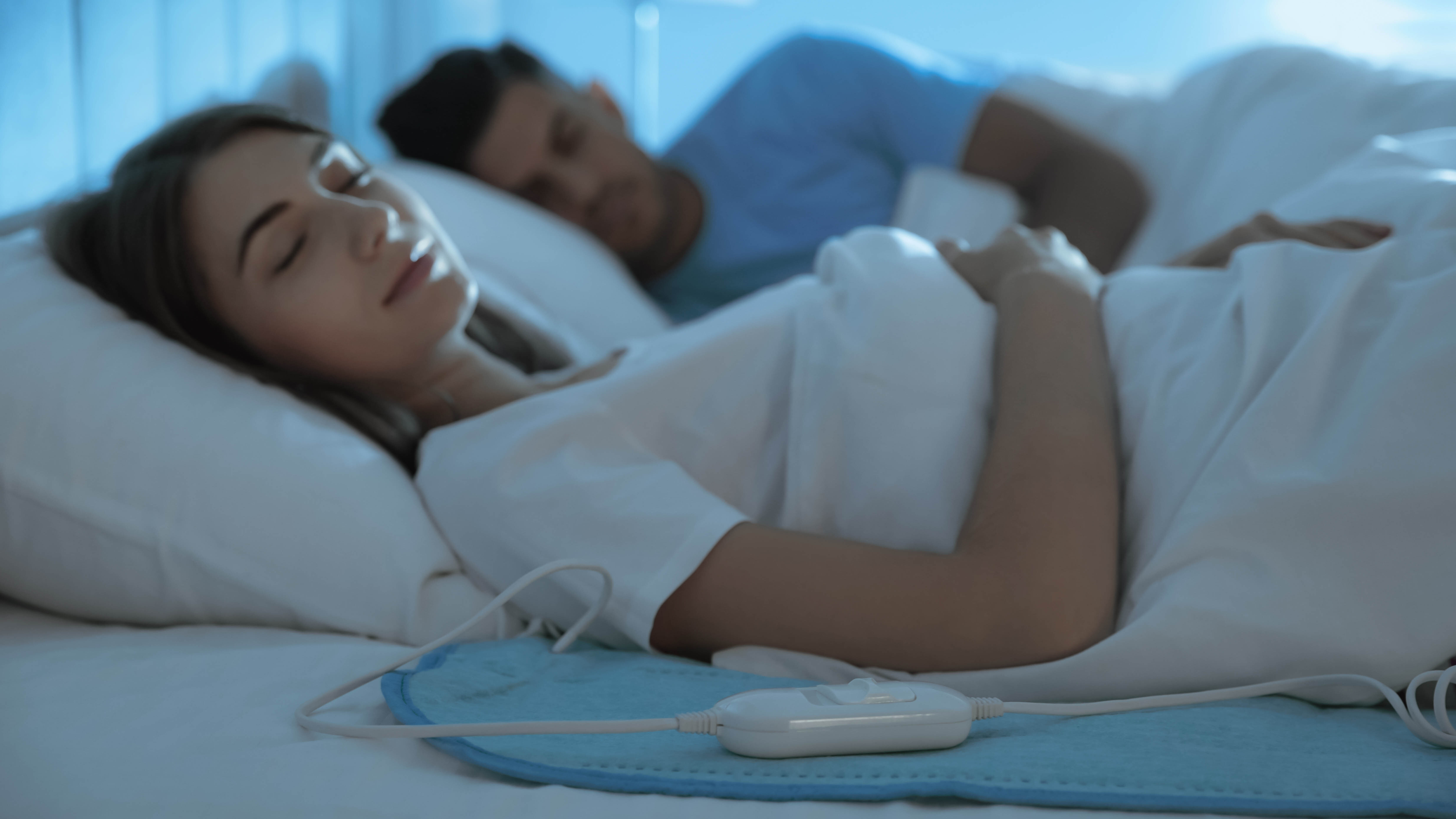 Homme et femme au lit, avec une femme au premier plan allongée sur une couverture électrique