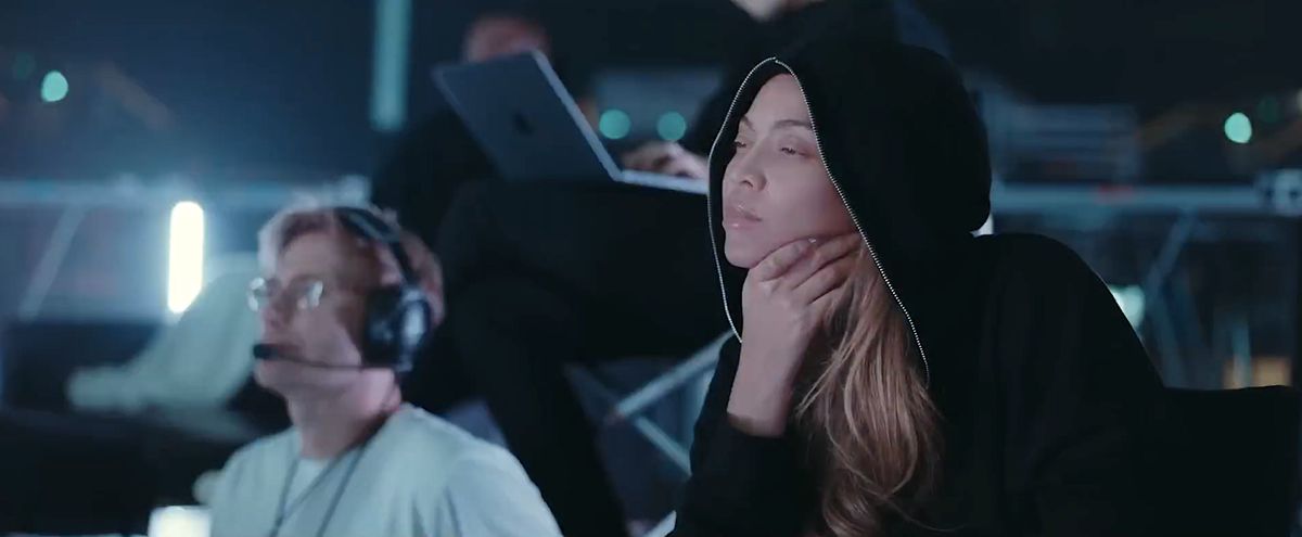 Beyoncé dans les coulisses de Renaissance : un film de Beyoncé, vêtue d'un sweat à capuche noir remonté sur la tête et assise parmi les techniciens alors qu'elle regarde quelque chose se dérouler hors écran